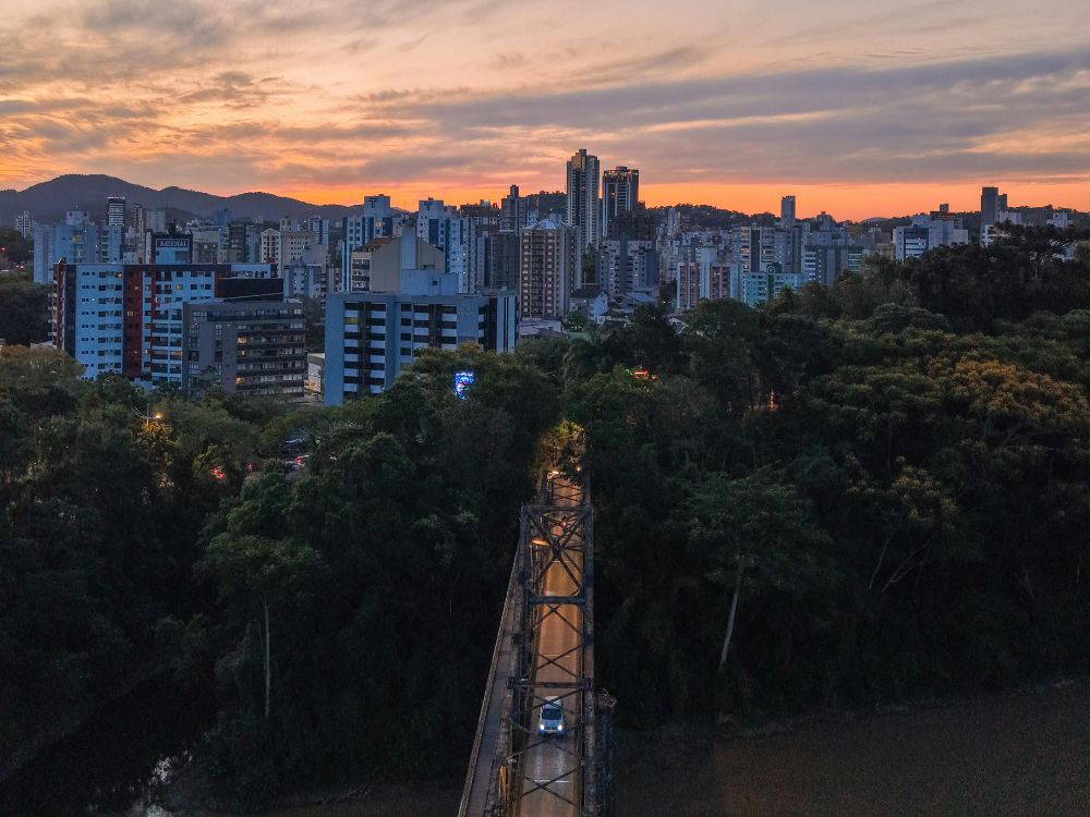 Vista aérea de Blumenau ao entardecer com ponte e prédios iluminados, cenário ideal para quem busca O que fazer em Blumenau à noite.
