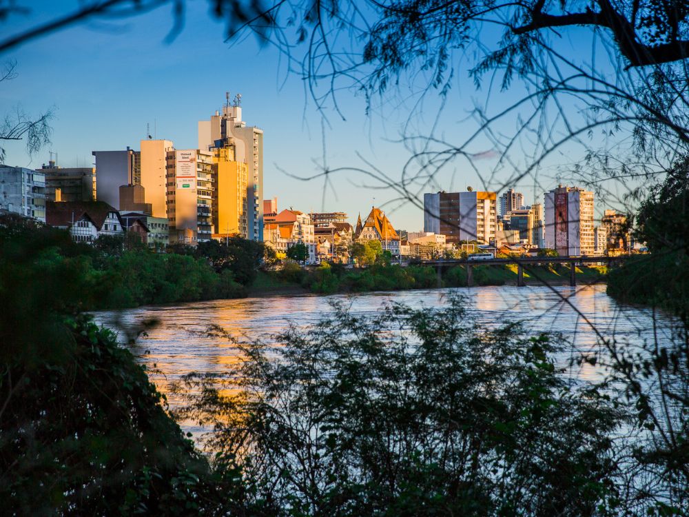 Vista urbana de Blumenau ao anoitecer com rio e prédios iluminados, perfeita para mostrar O que fazer em Blumenau à noite.