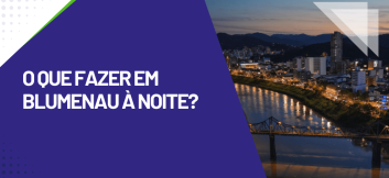 Vista noturna de Blumenau com rio iluminado, ponte metálica e prédios ao fundo, destaque turístico sobre O que fazer em Blumenau à noite.